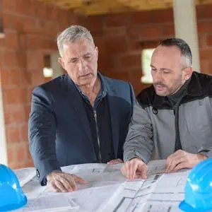 Two men in construction gear examining blueprints, emphasizing collaboration in the construction industry under employment law. -  Law Offices Of David S. Rich