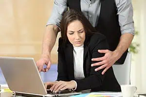 Man engaging in inappropriate behavior towards woman at her desk, representing sexual harassment